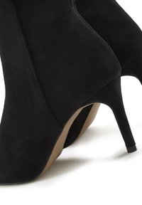 Stivaletti alla caviglia a tacco alto in suede nero caratterizzati da una punta affilata e un tacco affusolato, con una texture liscia e un design minimalista.