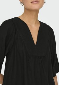 Top nero con scollatura a V, maniche 3/4 e dettagli arricciati sul busto; realizzato in un tessuto testurizzato.