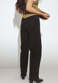 Käe kõrge mustad teksapüksid sirge lõikega. Omab kahte tagataskut ja nähtavat õmblust. Sile tekstuur, stiilitud kontsakingadega.