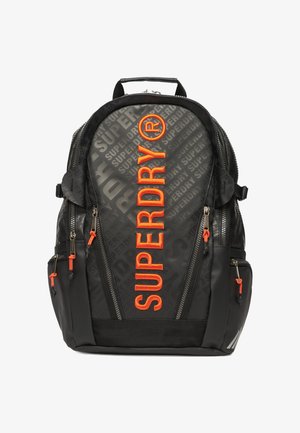 Zaino nero con motivo goffrato "SUPERDRY", logo arancione brillante, numerose tasche con cerniera e spallacci regolabili.