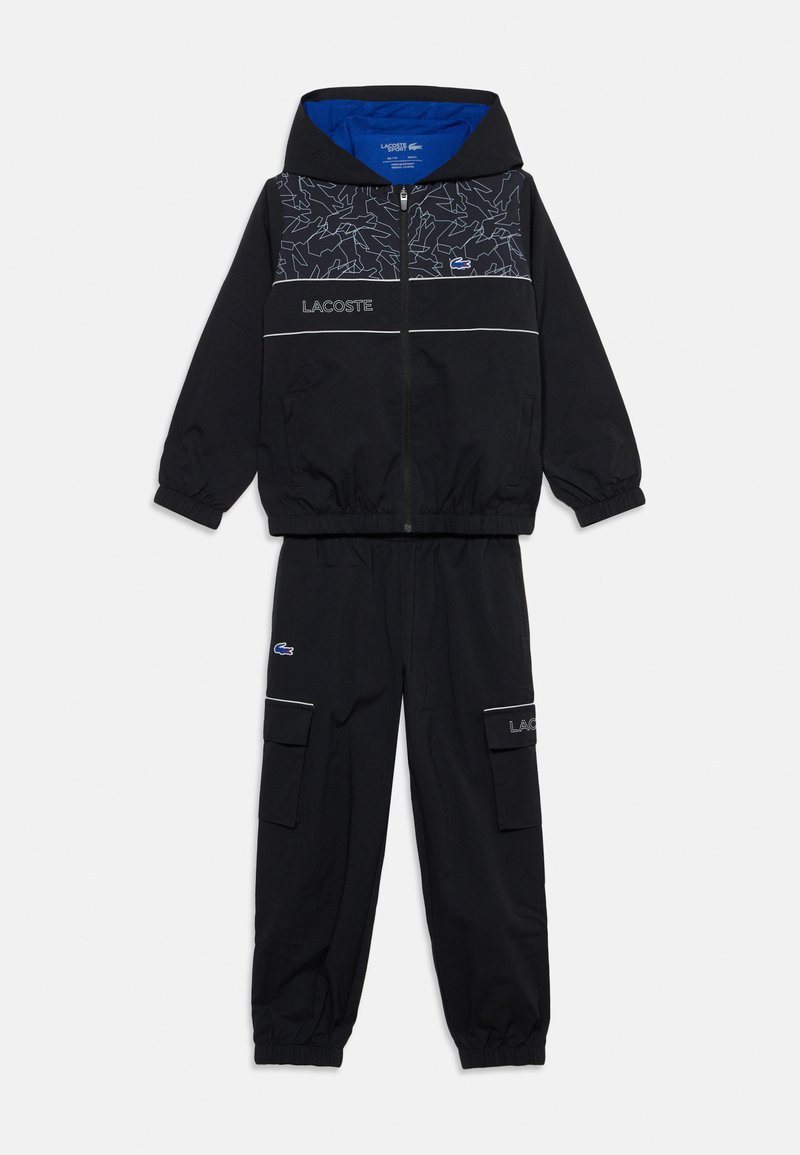Survêtement noir deux pièces avec veste zippée à capuche ornée d'un motif de lignes blanches et pantalon cargo noir avec poignets élastiqués et poches.