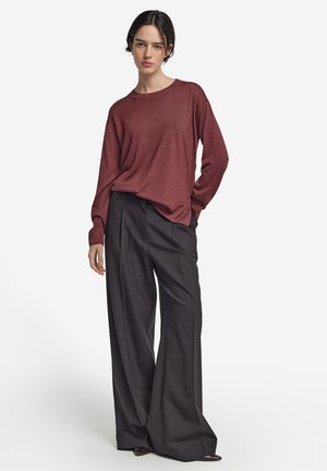 Bordeaux trui met een ronde hals en lange mouwen, gecombineerd met wijde grijze broek. De materialen lijken zacht en bieden een relaxte pasvorm.