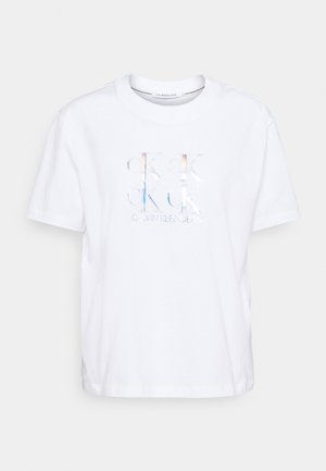 Weißes Calvin Klein Jeans T-Shirt mit kurzen Ärmeln, holografischem, sich wiederholendem "CK" Logo und Markennamen auf der Vorderseite.
