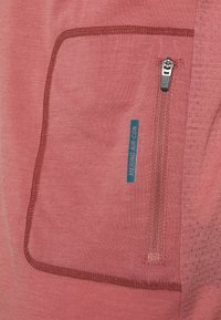 Prenda de lana merino en color rosa empolvado con superficie texturizada. Presenta un bolsillo con cremallera y costura en burdeos a contraste.
