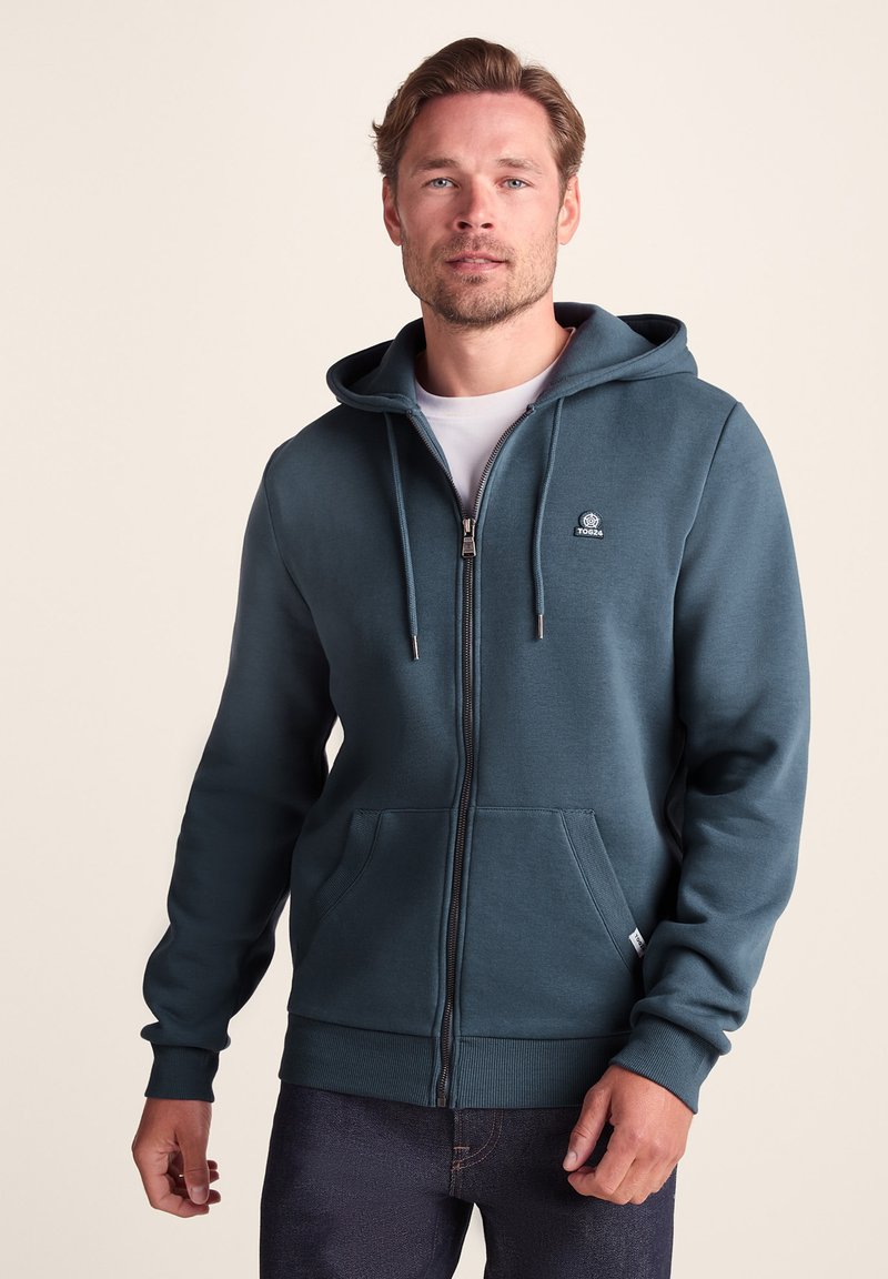 Hooded zip-up sweatshirt in dark teal, featuring a front kangaroo pocket, ribbed cuffs, and a logo detail on the chest. Soft fabric texture.