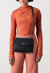 Sac à main en cuir noir à finition texturée, doté d'un rabat et d'une bandoulière chaîne. Orné d'une plaque logo métallique.