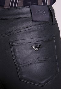 Svarta jeans med en slät yta. Har en präglad logotyppatch på midjan och en metallisk logotyp på bakfickan.