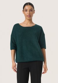 Teal oversized trui in een gestructureerde brei, met een brede neklijn en mouwen tot op de elleboog, gecombineerd met zwarte op maat gemaakte pantalons.