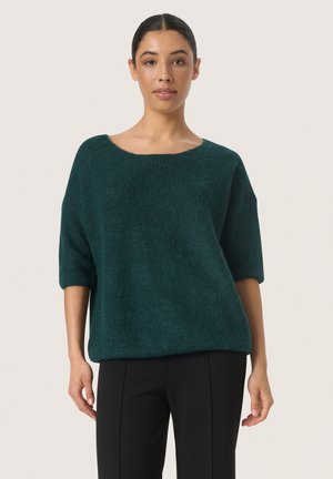 Teal oversized sweater i en struktureret strik, med en bred halsudskæring og ærmer til albuen, parret med sorte skræddersyede bukser.