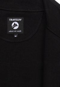 Zwarte kledinghalssnit met een label "TRAVELIN' where we walk" en een bijgevoegd maatlabel gemarkeerd met "M" voor medium.