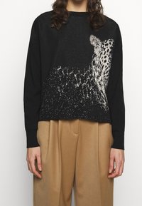 Czarny sweter z białym wzorem w panterkę, o luźnym kroju, z długimi rękawami, ściągaczami przy mankietach i krótkim fasonem. Lekko fakturowana tkanina.