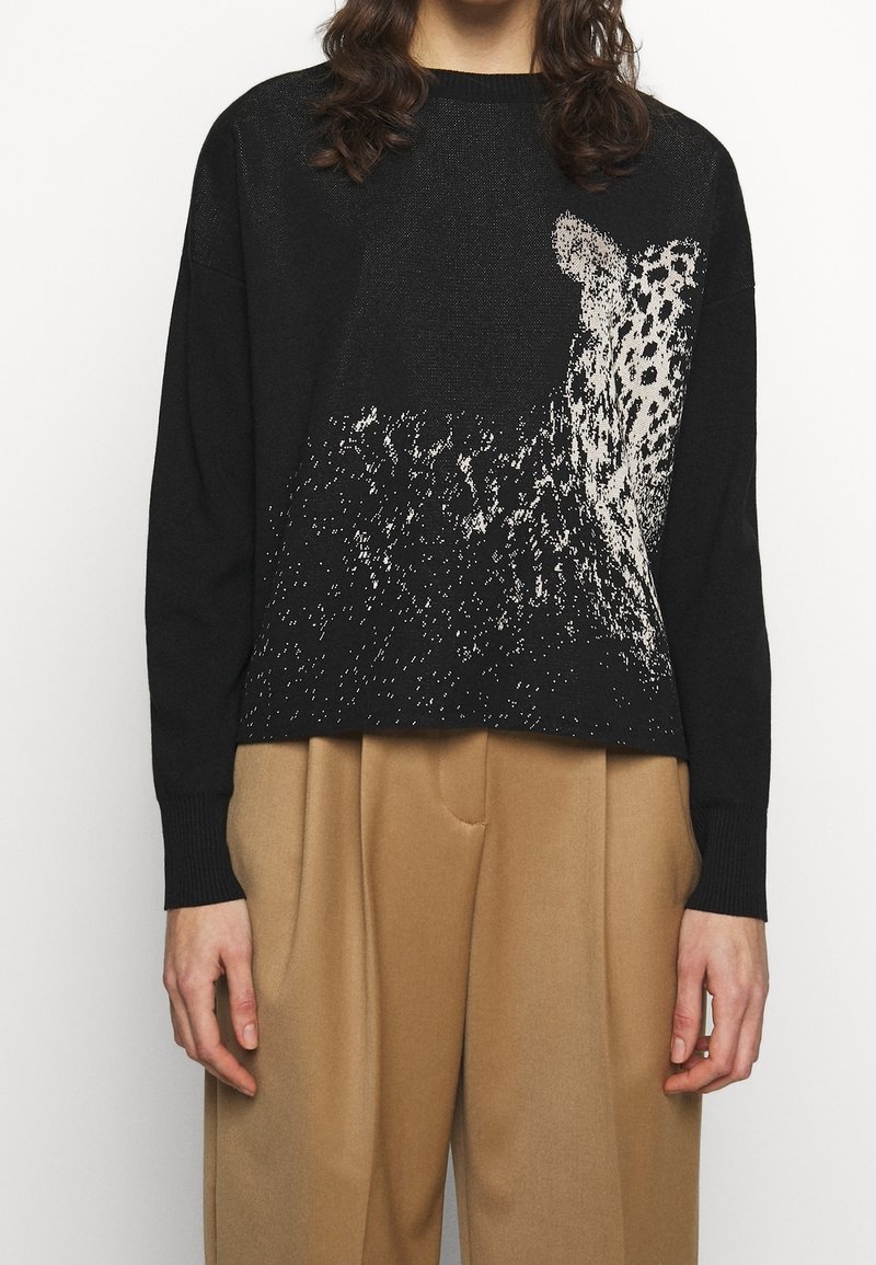 Czarny sweter z białym wzorem w panterkę, o luźnym kroju, z długimi rękawami, ściągaczami przy mankietach i krótkim fasonem. Lekko fakturowana tkanina.
