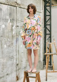 Blumenhemdkleid in Pastellfarben mit langen Ärmeln, Taillengürtel und lässiger Passform; aus leichtem Stoff, steht auf einem Hocker.