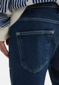 Mörkblå jeans i denim med design på bakfickan, utrustade med kontrasterande vita sömmar och en texturerad tygfinish.