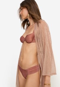 Σετ μπικίνι σε μεταλλικό ροζ με τοπ χωρίς τιράντες και ρυτιδωμένες πλευρές, συνδυασμένο με διάφανο, ελαφρύ κιμονό ανοιχτού μπροστινού μέρους.
