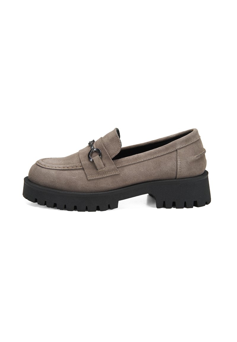 Grauer Wildlederslipper mit einer klobigen schwarzen Sohle, ausgestattet mit einem dekorativen Riemen und einem metallischen Akzent. Glatte Textur mit einem abgerundeten Zehenbereich.