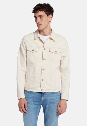 Giacca di jeans chiara con colletto, due tasche sul petto, bottoni in rame e tasche laterali a fessura. Indossata sopra una camicia bianca.