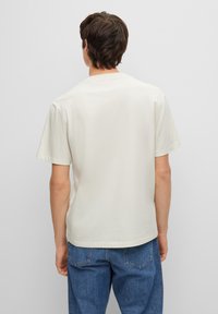 Camiseta blanca de manga corta con un corte relajado y cuello redondo. La tela parece suave y se combina con jeans de denim azul.