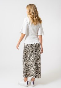 Top bianco arricciato abbinato a una lunga gonna con stampa leopardata. Sneakers bianche con accenti viola completano l'outfit. Tessuti morbidi e vestibilità comoda.