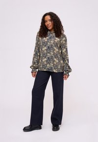 Blouse à manches longues à motif floral en bleu marine avec des accents crème, coupe décontractée, associée à un pantalon large noir et des chaussures noires.