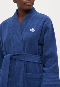 Ναυτικό μπλε μπουρνούζι από βελουτέ ύφασμα με ζώνη στη μέση, υφή στην επιφάνεια και κεντημένο λογότυπο "RL" στην αριστερή πλευρά του στήθους. Περιλαμβάνει πλαϊνές τσέπες.