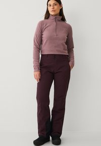 Fleece kvart-zip top i lyse lilla, parret med mørk burgunder bukser med knaplukning og sidelommer. Sorte fodtøj inkluderet.