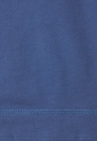 Blauwe katoenen stof met een gladde textuur. Wordt gekenmerkt door lichtblauwe stiksels langs de onderste zoom en een consistente breipatroon overal.
