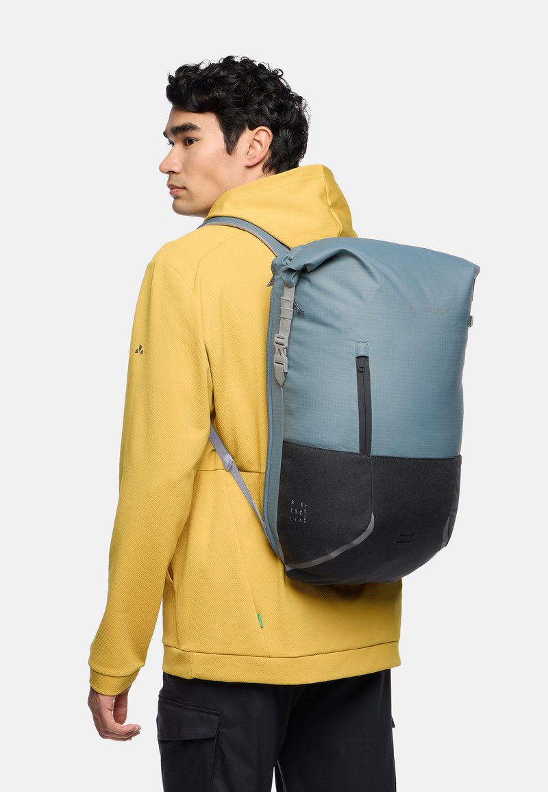 Rucksack mit einem Rolltop-Design, gefertigt aus blauem und grauem wasserdichtem Material, ausgestattet mit verstellbaren Trägern, einem flachen Boden und Logo-Akzenten.