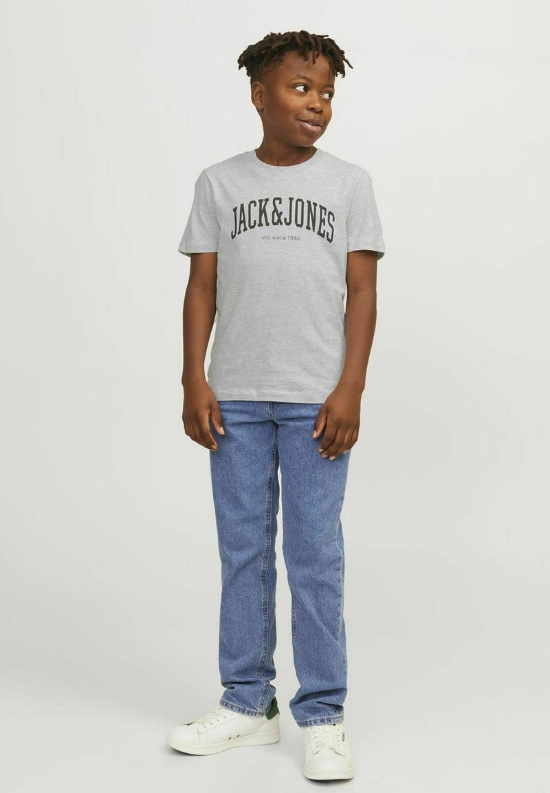 Camiseta gris de manga corta con gráfico negro "JACK & JONES", combinada con jeans de pierna recta azules y zapatillas blancas con acentos verdes.