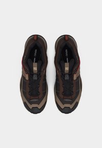 Ζευγάρι καφέ και μαύρα πεζοπορικά παπούτσια Salomon με σύστημα γρήγορου δέσιμου, ενθέματα Ortholite και ανθεκτικές σόλες, φωτογραφημένα από πάνω σε λευκό φόντο.