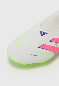 Botas de fútbol con parte superior blanca, plantilla en neón verde y acentos rosas. Presentan un diseño texturizado y un collar de calcetín removible para mayor comodidad.