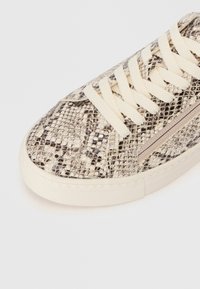 Αθλητικά παπούτσια με υφή σε σχέδιο κόμπρα σε κρέμα και καφέ απόχρωση. Διαθέτουν κρέμα κορδόνια και λεπτομέρεια με φερμουάρ στο πλάι. Λαστιχένια σόλα με ραφές.