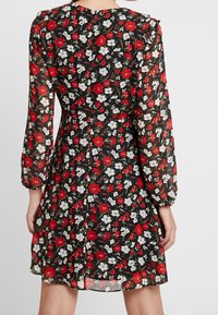 Blommig klänning med långa genomskinliga ärmar, svart bas, med röda vallmo och vita blommor. Volangiga axlar och detalj vid bakstängning synlig.