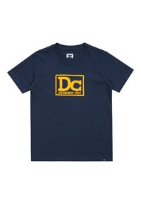 Mörkblå bomulls t-shirt med korta ärmar, med en gul rektangulär logotyp med "DC" och "SHOES-1994" i ett djärvt, kantigt typsnitt.