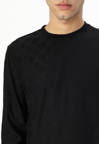 Black long-sleeve shirt featuring a textured pattern of symbols, with a round neckline and soft fabric, designed for a fitted appearance.