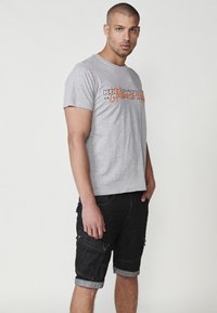 Gray cotton t-shirt with graphic print, paired with black denim shorts featuring cargo pockets and rolled cuffs.