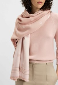 Długi różowy szalik z miękkiego materiału, z subtelny wzorem logo i frędzlami na brzegach, elegancko zarzucony na szyi.