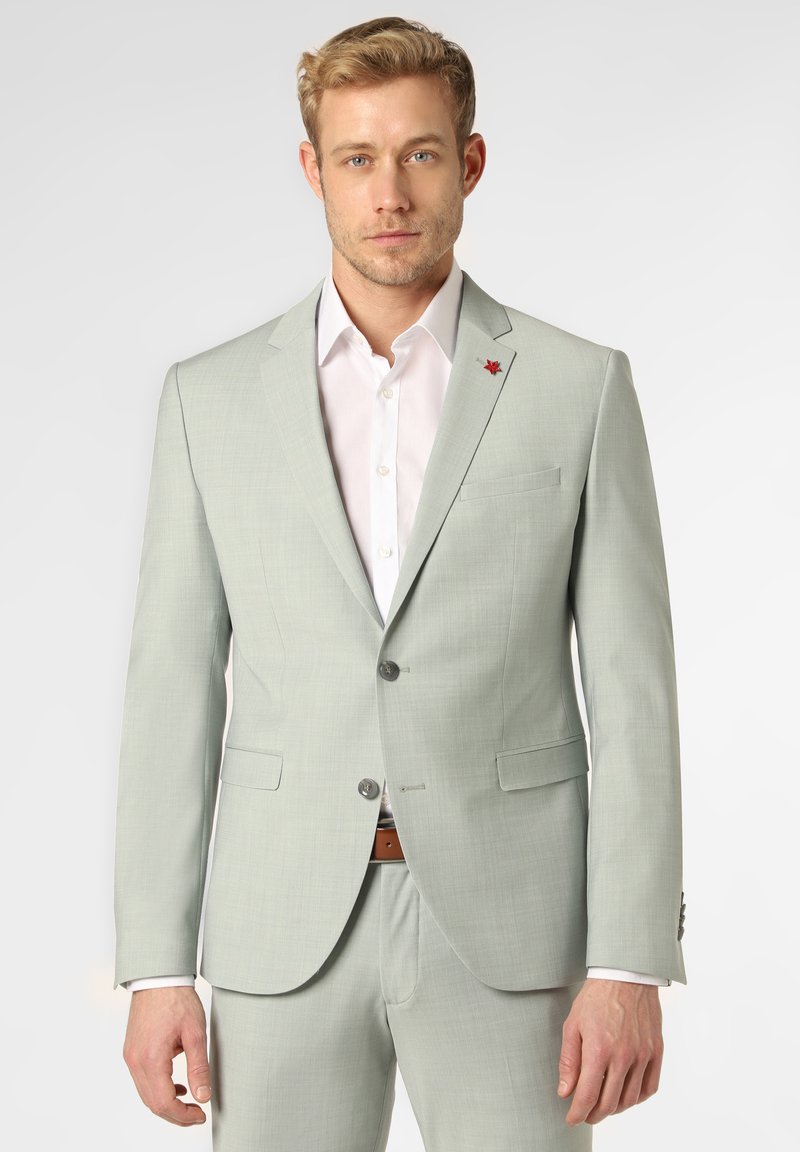 Hellgrüner Blazer mit strukturierter Oberfläche, zwei Knöpfen und einem kleinen roten Emblem auf dem Revers, kombiniert mit einem weißen Hemd und einem braunen Gürtel.