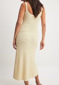 Knit midi-mekko pehmeässä kermavärissä, jossa on ribbikuvio ja kapeat olkaimet. Tiukka siluetti laskeutuu vyötäröltä liehuvaan helmaan, jossa on matala selkä.