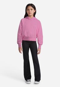 Ružová skrátená mikina s kapucňou, s raglánovými rukávmi, v kombinácii s čiernymi rozšírenými nohavicami a čiernymi teniskami s bielymi podrážkami.