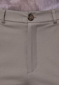 Gray fabric trousers with a smooth texture, featuring a brown button and a classic zipper fly. Visible stitching along the seams.