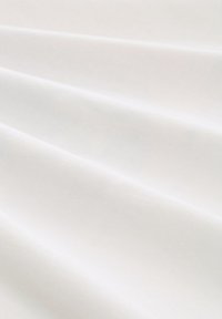 Witte stof met een gladde textuur, met zachte plooien en subtiele ribbels. Het oppervlak reflecteert het licht op een zachte manier, wat de puurheid en eenvoud benadrukt.