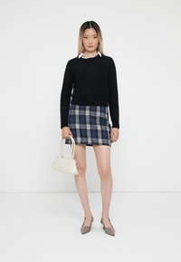 Schwarzer Pullover, blaues Karomuster-Minirock, cremefarbene Handtasche, taupefarbene, spitze Ballerinas. Glatte Textur, markante Muster und taillierte Passform.