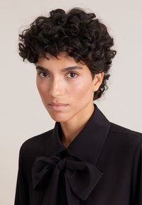 Schwarze Bluse mit einer großen Schleife am Kragen, glattes Material, klassisches Hemddesign und strukturierten Hemdkragen.