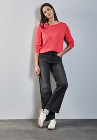 Pull en corail à manches longues, associé à un jean large taille haute noir. Modèle portant des baskets blanches avec des accents beiges.
