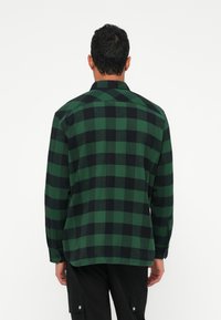 Camicia di flanella a quadri verde e nera con maniche lunghe e polsini abbottonati, caratterizzata da un colletto classico e un orlo dritto.