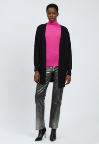 Sort cardigan over en lyserød turtle neck, parret med skinnende sølv bukser og sorte højhælede støvler. Glat tekstur og tætsiddende design.