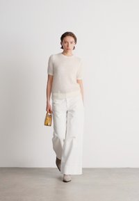 Svetlý, textúrovaný pletený sveter v odtieňoch off-white s krátkymi rukávmi, skombinovaný s bielymi nohavicami s vysokým pásom a malou žltou kabelkou.