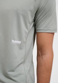 Hellgraues Kurzarm-Sportshirt aus strukturiertem Material mit einem weißen "hummel PERFORMANCE" Logo auf der linken Seite.