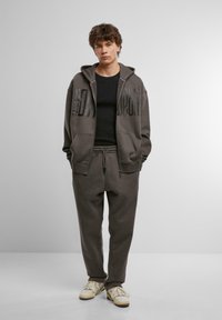 Hættegrå sweatshirt med stort tryk, parret med matchende sweatpants med elastisk talje og lommer. Struktureret stof.